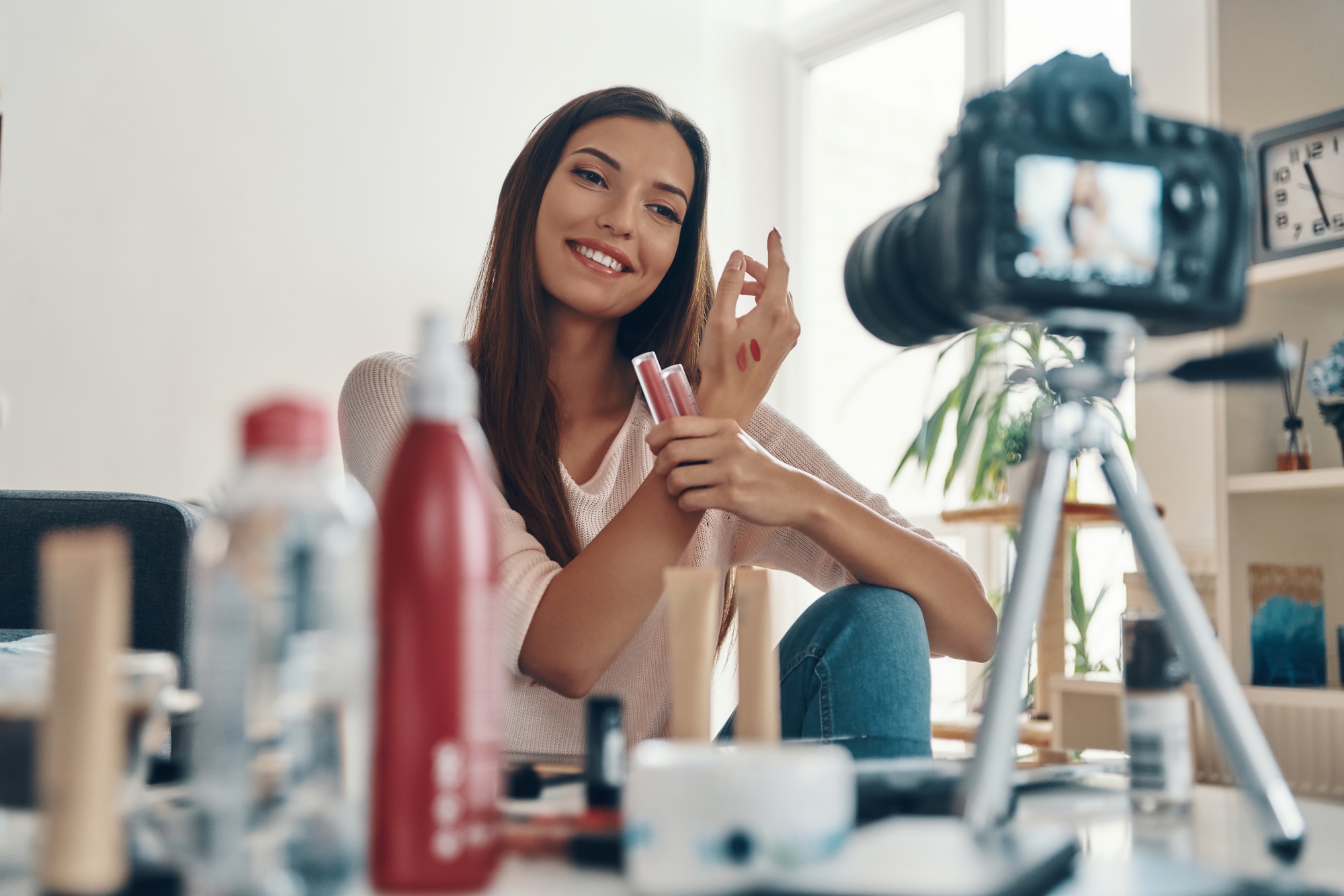 Stunning young woman applying lip gloss and smiling while making social media video